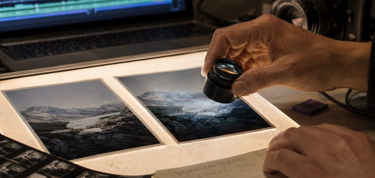 Photographer comparing original and AI-altered prints with a loupe to inspect a faint digital watermark.